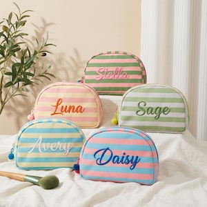Puede incluir: Cinco neceseres a rayas en colores pastel, cada uno bordado con un nombre diferente: Luna, Stella, Sage, Avery y Daisy. Los neceseres tienen forma redondeada, cierre de cremallera y un pequeño pompón.