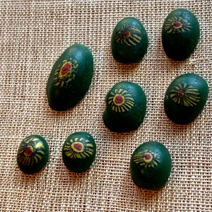 Puede incluir: Ocho piedras verdes con diseños pintados en amarillo y rojo. Las piedras son redondas y ovaladas y tienen una superficie lisa y pulida.