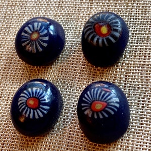 May include: Four dark blue ceramic buttons with white and orange flower designs. The buttons have a glossy finish.