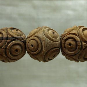 May include: Three wooden beads with a carved spiral design. The beads are a light brown color with darker brown grain patterns. Each bead has a small hole drilled through the center.