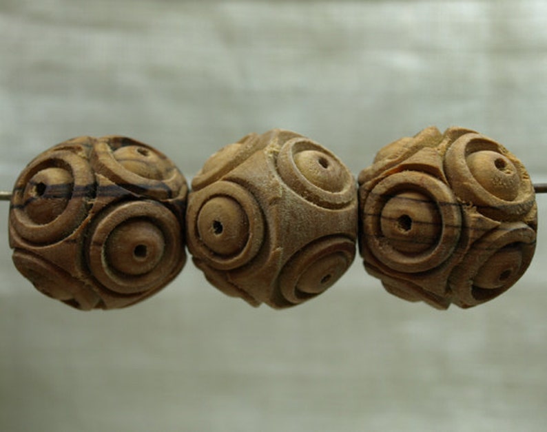 May include: Three wooden beads with a carved spiral design. The beads are a light brown color with darker brown grain patterns. Each bead has a small hole drilled through the center.