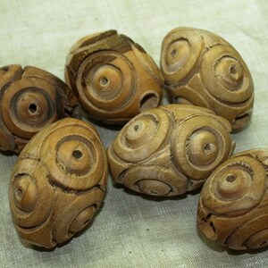 May include: Six wooden beads with intricate circular carvings. The beads are a light brown color and have a smooth, polished finish.