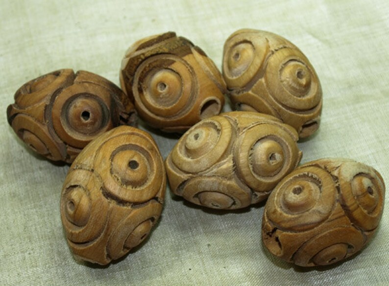 May include: Six wooden beads with intricate circular carvings. The beads are a light brown color and have a smooth, polished finish.