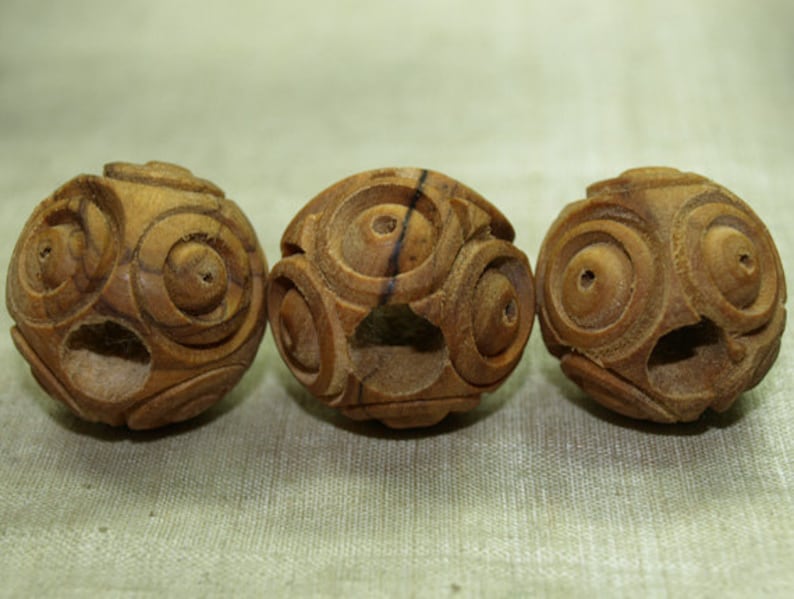 May include: Three intricately carved wooden spheres. Each sphere is a warm brown color and features a series of concentric circles and geometric patterns. The spheres are evenly spaced, showcasing the detailed craftsmanship.