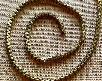 Könnte beinhalten: Eine goldene Kettenkette mit einem Gliederketten-Design. Die Kette ist spiralförmig auf einem beigefarbenen Stoffhintergrund aufgerollt.
