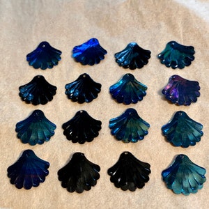 May include: A collection of 15 iridescent blue and black seashell-shaped embellishments. The embellishments are arranged in three rows of five.