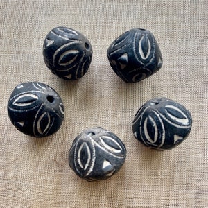 May include: Five black ceramic beads with white geometric designs. The beads are round and have a hole in the center.