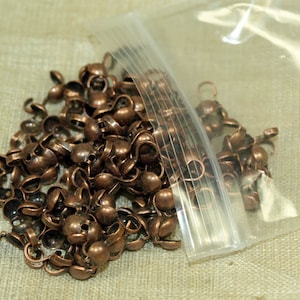 May include: A plastic bag filled with a large quantity of small, copper-colored metal caps with a loop on the top. The caps are used for jewelry making or other craft projects.