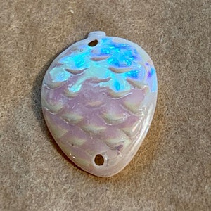 May include: A white iridescent ceramic ornament shaped like a pine cone with two holes for hanging.