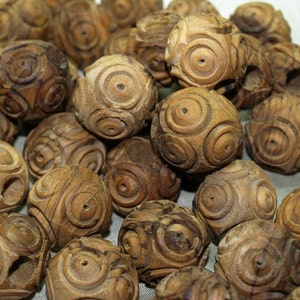 May include: A collection of intricately carved wooden spheres. Each sphere features a series of concentric circular patterns, creating a detailed and textured surface. The wood has a warm, natural brown tone, and the spheres vary slightly in size.