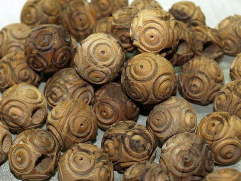 May include: A collection of intricately carved wooden spheres. Each sphere features a series of concentric circular patterns, creating a detailed and textured surface. The wood has a warm, natural brown tone, and the spheres vary slightly in size.