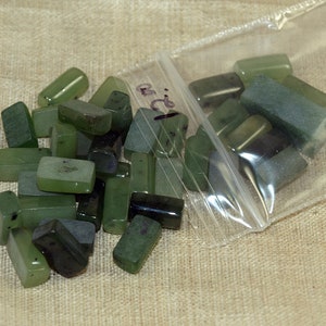 May include: A plastic bag filled with green jade stones. The stones are rectangular and have a smooth, polished finish.