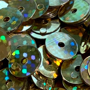 May include: A pile of iridescent green and blue sequins with a metallic finish. The sequins are round with a hole in the center.
