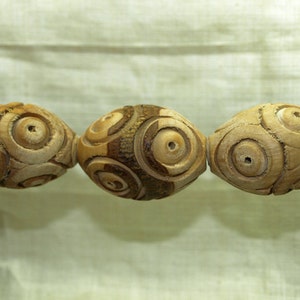 May include: Three wooden beads with a circular pattern carved into the surface. The beads are light brown and have a natural wood finish.