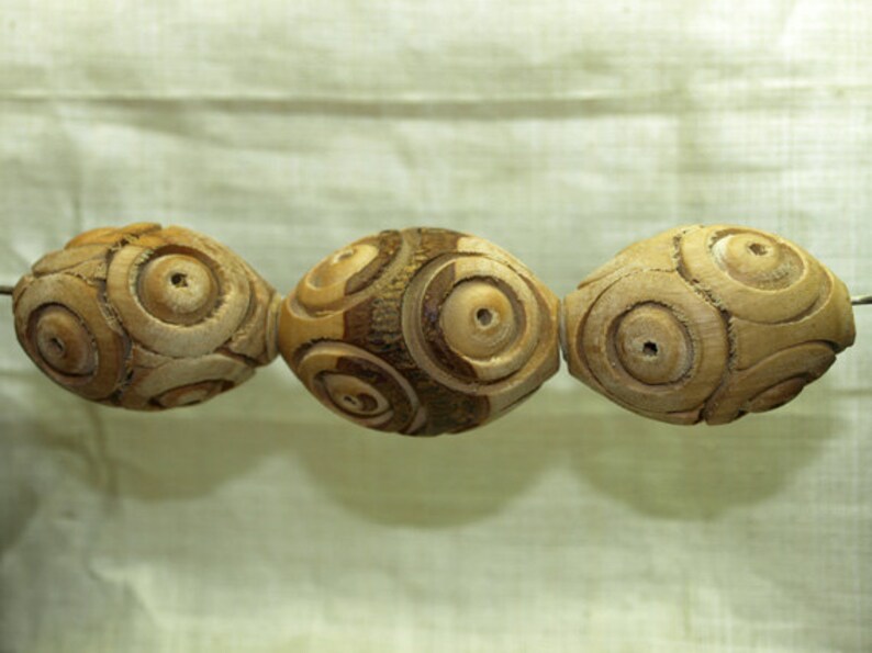 May include: Three wooden beads with a circular pattern carved into the surface. The beads are light brown and have a natural wood finish.