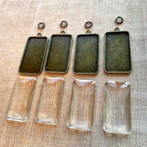 May include: Four rectangular metal frames with clear glass inserts. The frames are a dark bronze color and have a loop at the top for hanging. The glass inserts are clear and smooth.
