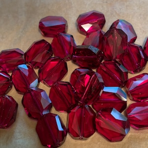 May include: A group of deep red faceted glass beads. The beads are oval shaped and have a shiny, polished finish.