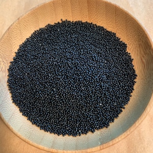 Puede incluir: Un bol lleno de pequeñas cuentas de semillas negras. Las cuentas son redondas y tienen un acabado liso y brillante.