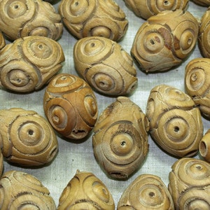 May include: A collection of wooden beads with a carved circular pattern. The beads are light brown in color and have a smooth, polished finish.