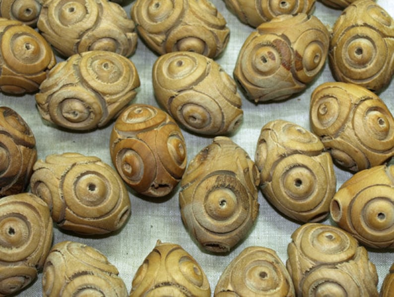 May include: A collection of wooden beads with a carved circular pattern. The beads are light brown in color and have a smooth, polished finish.
