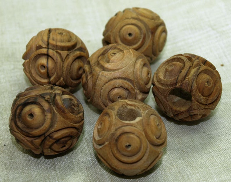 May include: Six small, intricately carved wooden spheres. Each sphere features a repeating pattern of concentric circles and a natural wood grain finish. The spheres are arranged on a light-colored surface, showcasing the detailed craftsmanship.