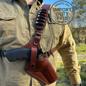 Könnte beinhalten: Ein Schulterholster-System aus braunem Leder mit einer geformten Pistolentasche mit Druckknopf-Sicherungsriemen und einem integrierten Munitionshalter am Schultergurt, der sieben einzelne Patronen in einer vertikalen Reihe hält.