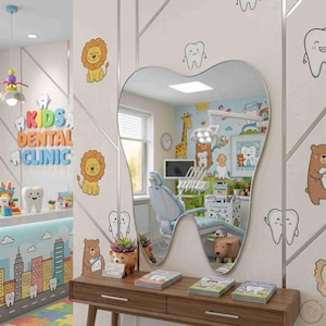 May include: A tooth-shaped wall mirror mounted above a wooden console table. The mirror reflects a pediatric dental office with a dental chair, medical equipment, and colorful wall decals of cartoon animals and teeth in a bright room.