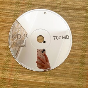 May include: A reflective CD-R disc with the text "CD-R COMPACT disc Rewritable High Speed" and "700 MB" printed on the surface. The disc reflects the image of a hand holding a phone.