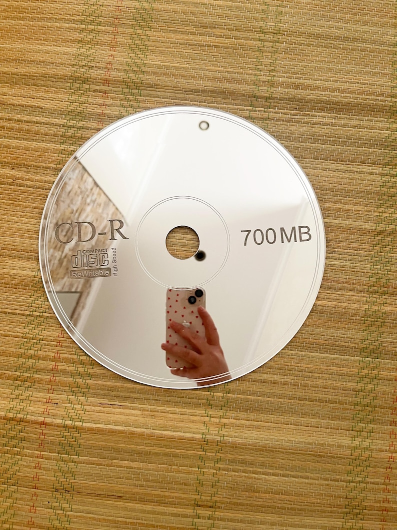 May include: A reflective CD-R disc with the text "CD-R COMPACT disc Rewritable High Speed" and "700 MB" printed on the surface. The disc reflects the image of a hand holding a phone.