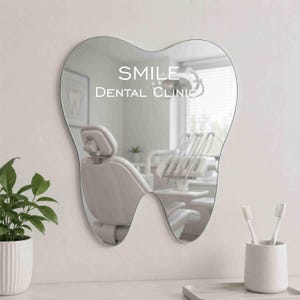 May include: A tooth-shaped wall mirror featuring the white text SMILE DENTAL CLINIC printed on the reflective surface. The mirror reflects a dental office interior, including a dental chair and equipment, with smooth, curved edges and a clear finish.