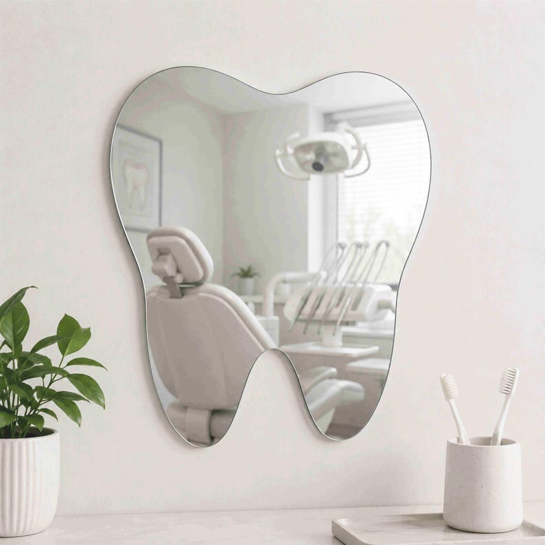 May include: A wall-mounted mirror shaped like a human tooth with a smooth, reflective surface. The mirror reflects a dental office interior, including a dental chair and overhead lighting equipment, providing a clear view of the room's contents.