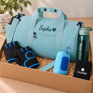 Könnte beinhalten: Eine hellblaue Sporttasche mit dem Namen Sophie und einem Herz auf der Vorderseite, dazu schwarze fingerlose Handschuhe, ein blauer Netzbeutel, eine dunkelgrüne Trinkflasche mit der Aufschrift Good State und ein schwarzes Armband mit Cicodaa.