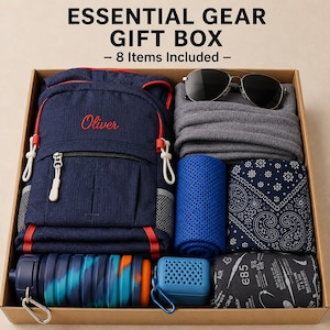 Op de afbeelding: Een kartonnen geschenkdoos met het label ESSENTIAL GEAR GIFT BOX - 8 Items Included met een marineblauwe rugzak met de naam Oliver, grijs fleece, een zwarte zonnebril, een blauwe koelhanddoek, een blauwe doek, een waterfles en een luidspreker.