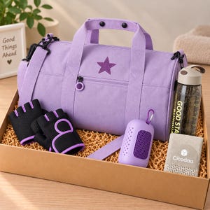 Könnte beinhalten: Eine lavendelfarbene Sporttasche mit Sternemblem, schwarze fingerlose Trainingshandschuhe mit violettem Rand, ein violettes Silikonetui mit Karabiner, eine transparente Trinkflasche mit dem Text GOOD STAR und ein beiges Handtuch mit dem Namen Cicodaa.