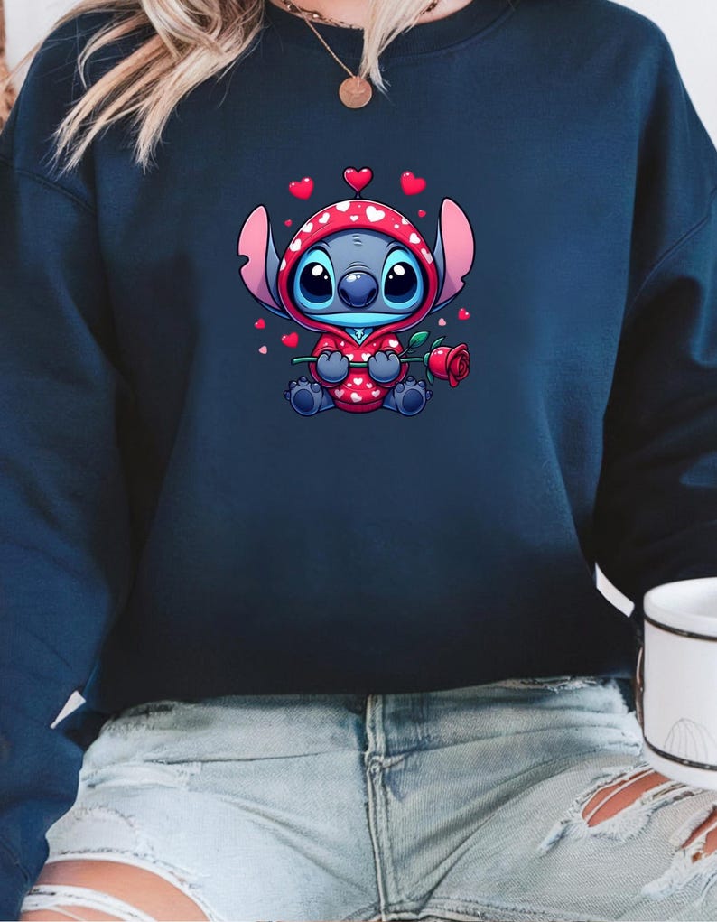 Op de afbeelding: Marineblauwe sweatshirt met een stripfiguur in een rode hoodie met witte harten. Het personage houdt een rode roos vast. Kleine rode harten zweven rond het personage. De sweatshirt wordt door een persoon gedragen.