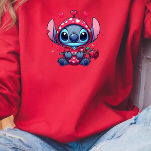 Op de afbeelding: Rode sweatshirt met een stripfiguur in een rood-witte hoodie met hartjespatroon, met een rode roos in de hand. Het personage heeft grote blauwe ogen en is omringd door zwevende harten. De sweatshirt is effen rood.