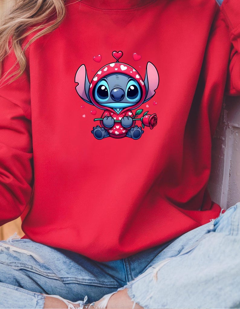Op de afbeelding: Rode sweatshirt met een stripfiguur in een rood-witte hoodie met hartjespatroon, met een rode roos in de hand. Het personage heeft grote blauwe ogen en is omringd door zwevende harten. De sweatshirt is effen rood.