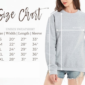 Op de afbeelding: Een lichtgrijs unisex sweatshirt met een maattabel. De tabel geeft de afmetingen voor breedte, lengte en mouwlengte in inches voor de maten S tot en met 2XL. De sweatshirt wordt gemeten op breedte, lengte en mouwlengte.