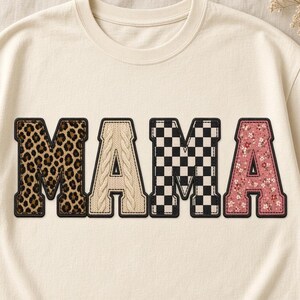 May include: A cream-coloured crewneck t-shirt featuring the word MAMA in large block letters. Each letter has a distinct pattern: the first M is leopard print, the first A is beige cable knit, the second M is black and white checkerboard, and the final A is pink with a small white floral print.