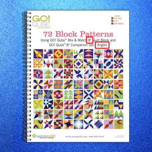 May include: Spiral-bound book titled "72 Block Patterns" with colorful quilt block designs. The cover features the "GO! Qube" logo and text indicating the use of 8-inch quilt blocks and angles. The book is on a blue surface.