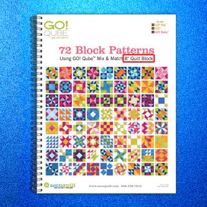 May include: A spiral-bound book titled "72 Block Patterns" featuring colorful quilt block designs. The cover text includes "GO! Qube" and "8" Quilt Block." The book showcases various geometric patterns in vibrant colors, ideal for quilting projects.
