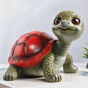 May include: A turtle figurine featuring a bright red, segmented shell and a textured, light green body. The turtle has large, dark, glossy eyes and a smiling expression, with detailed scales on its head and legs, standing in a forward-facing pose.
