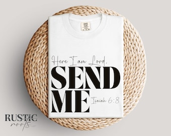 May include: A white t-shirt with the text "Here I am Lord, SEND ME Isaiah 6:8" in black. The shirt is folded and placed on a round, woven, light brown surface. The brand name "RUSTIC roots" is at the bottom left.