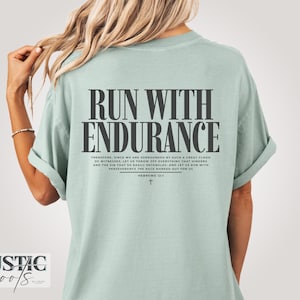 Op de afbeelding: Lichtgroen t-shirt met de tekst "RUN WITH ENDURANCE" in grote, donkere letters. Daaronder een bijbelvers en een kruis. Het shirt heeft een comfortabele, casual stijl en is van katoen.