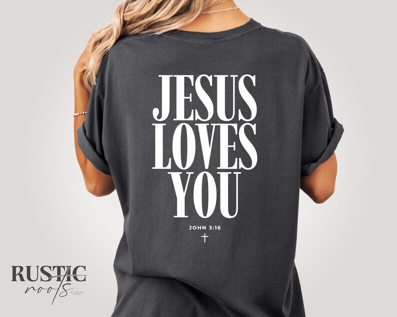 May include: Dark gray t-shirt with the text "JESUS LOVES YOU" in large white letters. Below the text is "JOHN 3:16" and a small cross. The shirt has rolled-up sleeves.