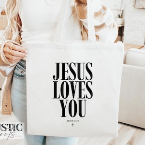May include: A white tote bag with the text "JESUS LOVES YOU" in large black letters. The text "JOHN 3:16" and a small cross are below the main text. The bag has white handles.