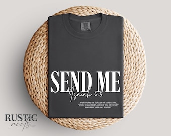 May include: Dark gray t-shirt with the words "SEND ME" in large white letters, with "Isaiah 6:8" below. The shirt is displayed on a round woven mat. The text "THEN I HEARD THE VOICE OF THE LORD SAYING, 'WHOM SHALL I SEND? AND WHO WILL GO FOR US?' AND I SAID, 'HERE AM I, SEND ME'" is also printed on the shirt.