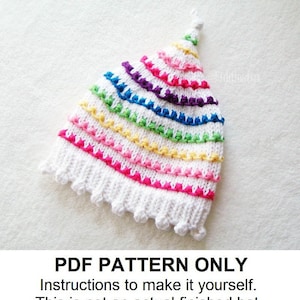 May include: A white knitted hat with a rainbow stripe pattern. The hat has a pointed top and a scalloped edge. PDF PATTERN ONLY. Instructions to make it yourself. This is not an actual finished hat.