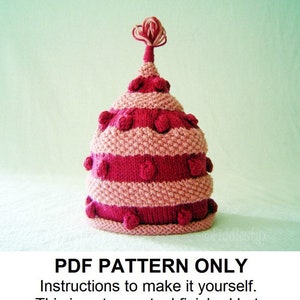 Op de afbeelding: Een roze en rode gebreide muts met een puntige top en een pompon. De muts heeft een gestreept patroon en is versierd met kleine, ronde, gebreide ballen. "PDF PATTERN ONLY Instructions to make it yourself. This is not an actual finished hat."
