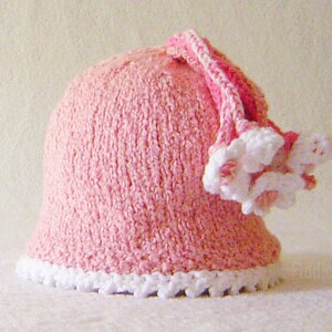 Puede incluir: Un gorro de crochet rosa con un borde blanco de crochet y un adorno de flor de crochet rosa y blanco.